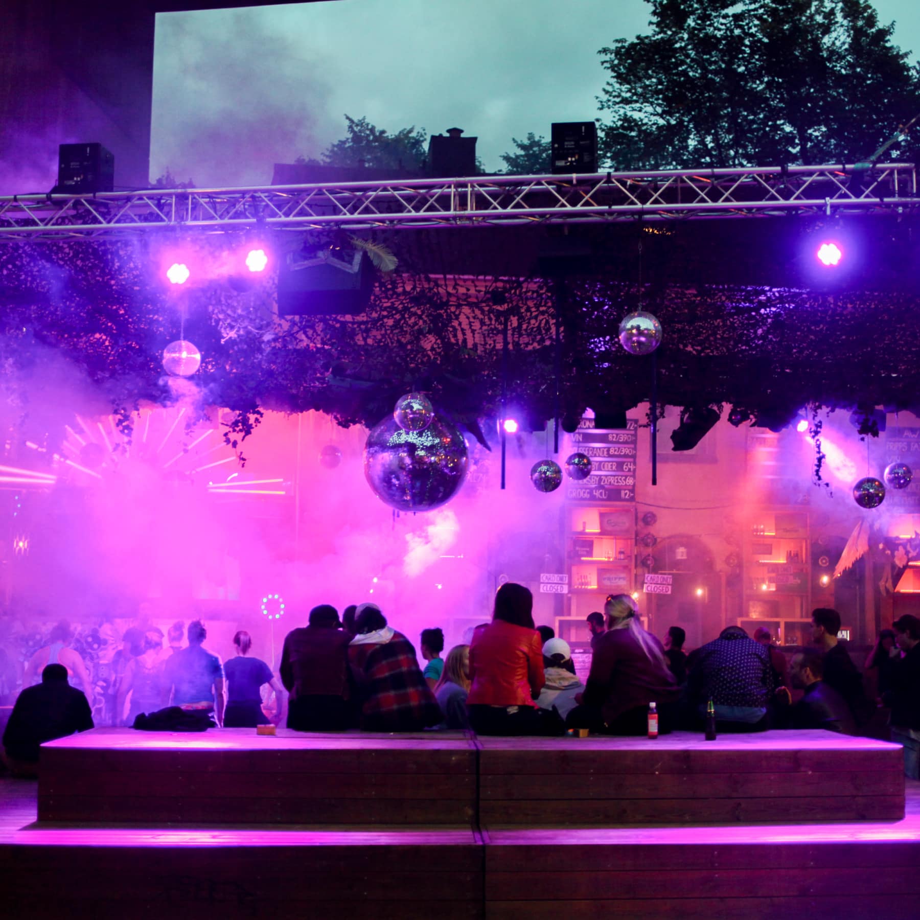 Live music in the centre of Stockholm, with a pink light hue amongst the people and smoke surrounding