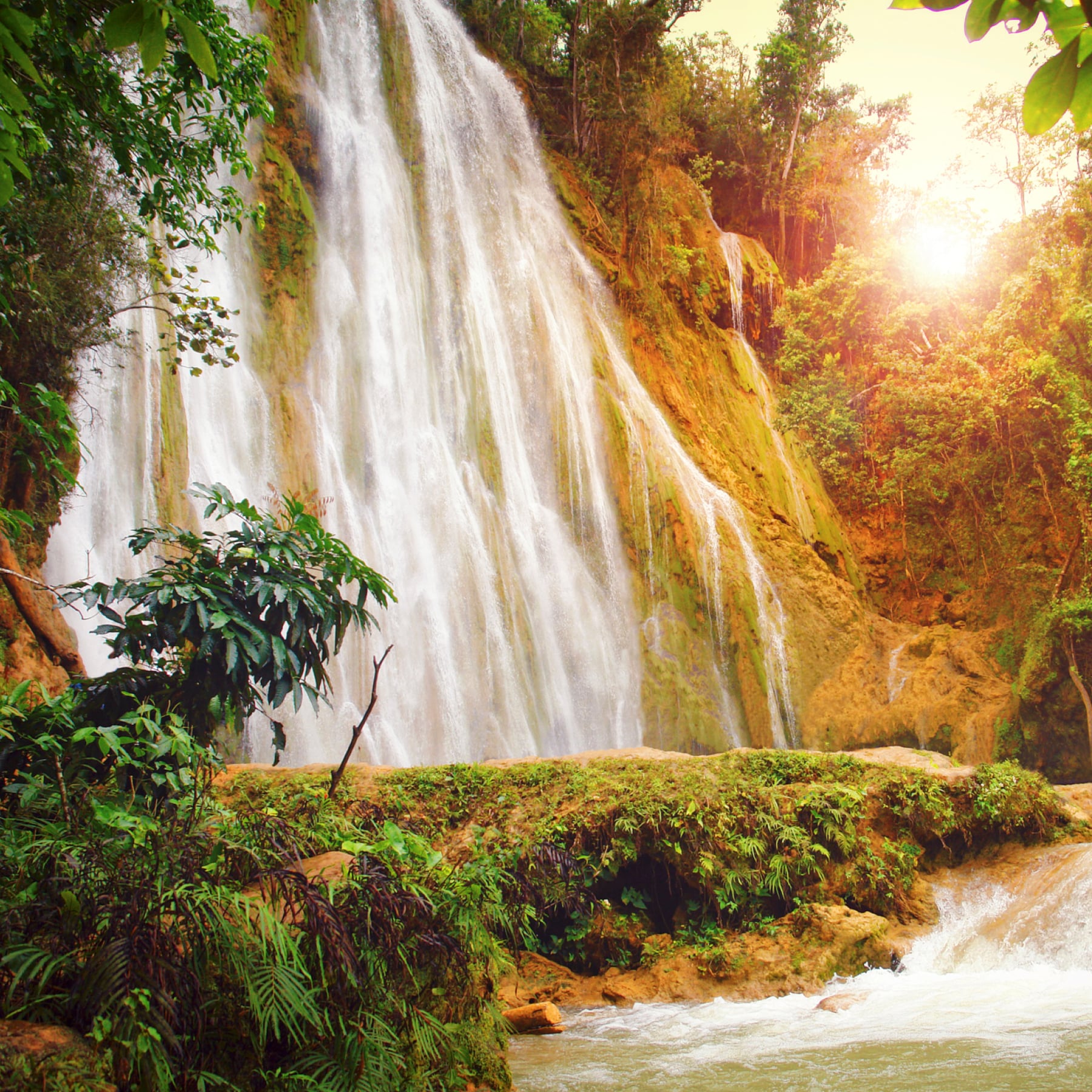 A waterfall in Dominican Republic with the sun peaking through the haze